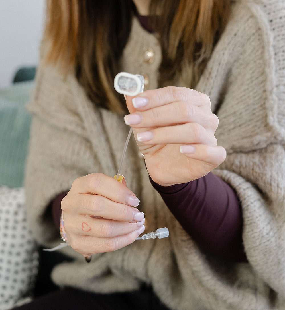 Nahaufnahme einer Beraterin, die auf einem Sofa sitzt und eine Portnadel in den Händen hält, um die sichere Anwendung bei der Versorgung von Portsystemen zu erklären.